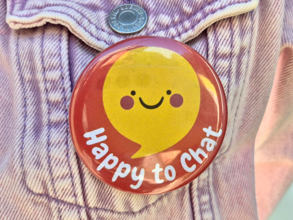 A Happy to Chat badge pinned to a denim jacket.